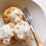 A close up of green chili cheddar biscuits and gravy with a fork.