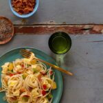 Breakfast pasta on a plate with a fork next to a drink and extra toppings.