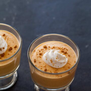 A close up of pumpkin mousse with a dollop of whipped cream and crumbled ginger snaps.