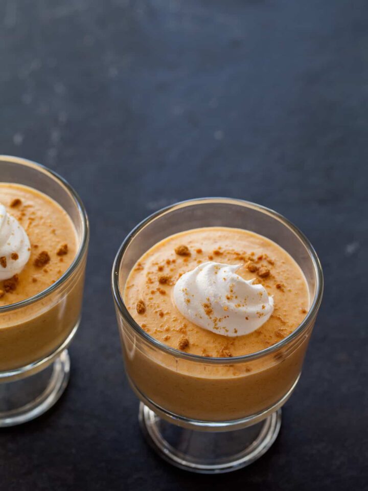 A close up of pumpkin mousse with a dollop of whipped cream and crumbled ginger snaps.