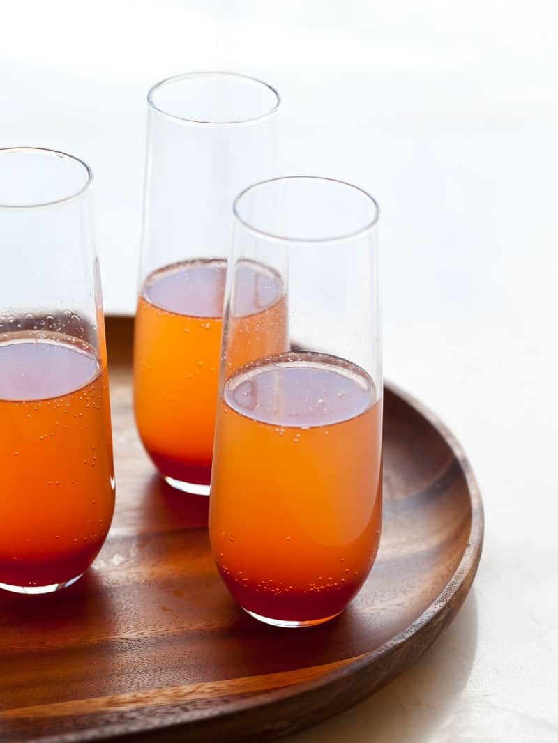 A glasses of spicy blood orange champagne punch on a wooden tray.