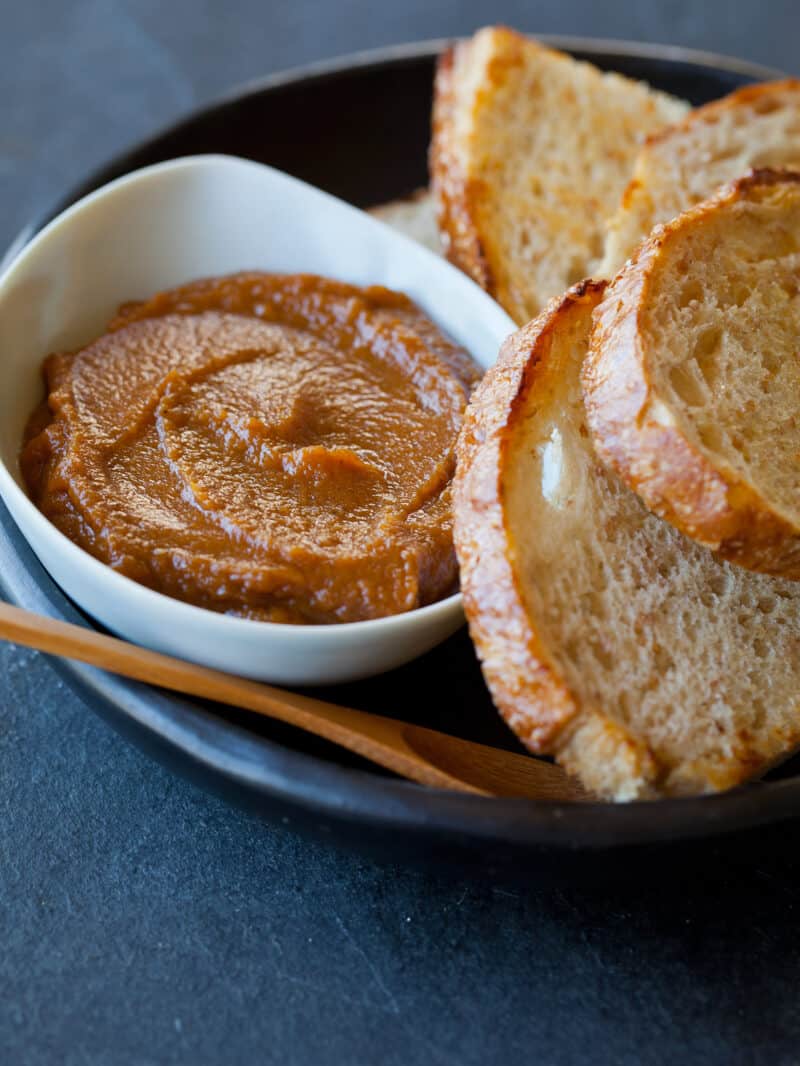 A close up of a bowl of sweet pumpkin butter on a plate of bread.