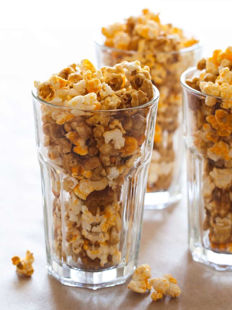 A close up of tall glasses full of cheddar and caramel popcorn mix.