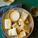 A plate of baby chimichangas with a bowl of sriracha lime dipping sauce.