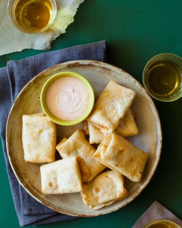 A plate of baby chimichangas with a bowl of sriracha lime dipping sauce.