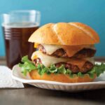 A close up of a double fifty fifty burger with a drink and paper towel.