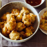 Bowls of shrimp fritters and dipping sauce on a napkin.