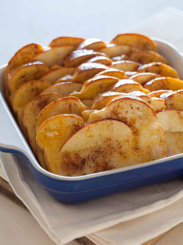 Baked apple french toast in a blue baking dish on a napkin.