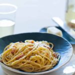 A bowl of basic pasta carbonara with a small plate of cheese and a microplane.