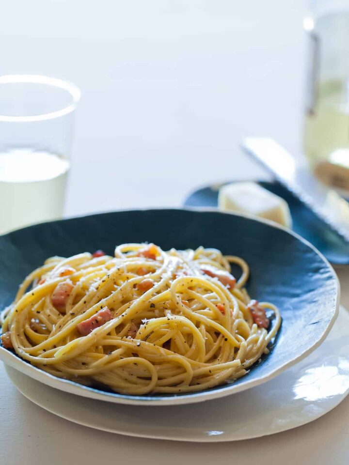 A bowl of basic pasta carbonara with a small plate of cheese and a microplane.