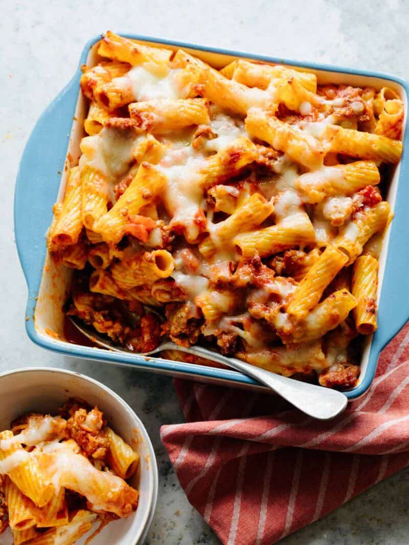 Baked Ziti in a baking dish with a scoop out and in a bowl. 