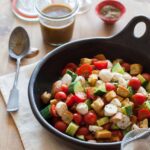 Panzanella salad in a serving bowl with a jar of dressing and a spoon.