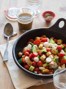Panzanella salad in a serving bowl with a jar of dressing and a spoon.