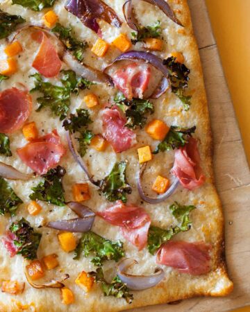 A close up of prosciutto kale butternut squash pizza on a wooden cutting board.