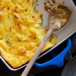 A blue pan of jalapeño cheddar corn spoon bread with a wooden spoon.