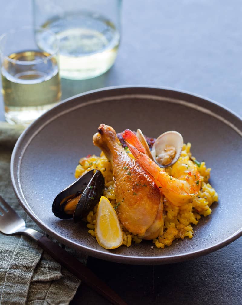 A bowl paella with a drink, napkin, and fork.