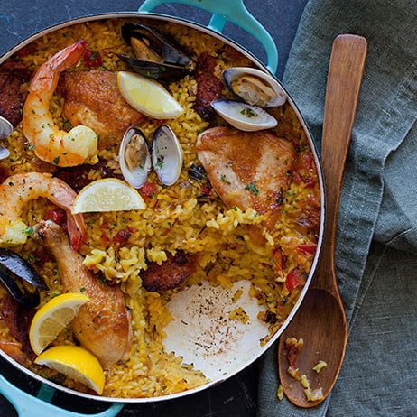 Paella in a pot pot with a scoop taken out and a wooden spoon next to it. 