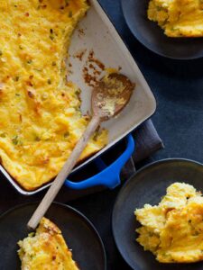 Jalapeño cheddar corn spoon bread with servings on small plates and a wooden spoon.