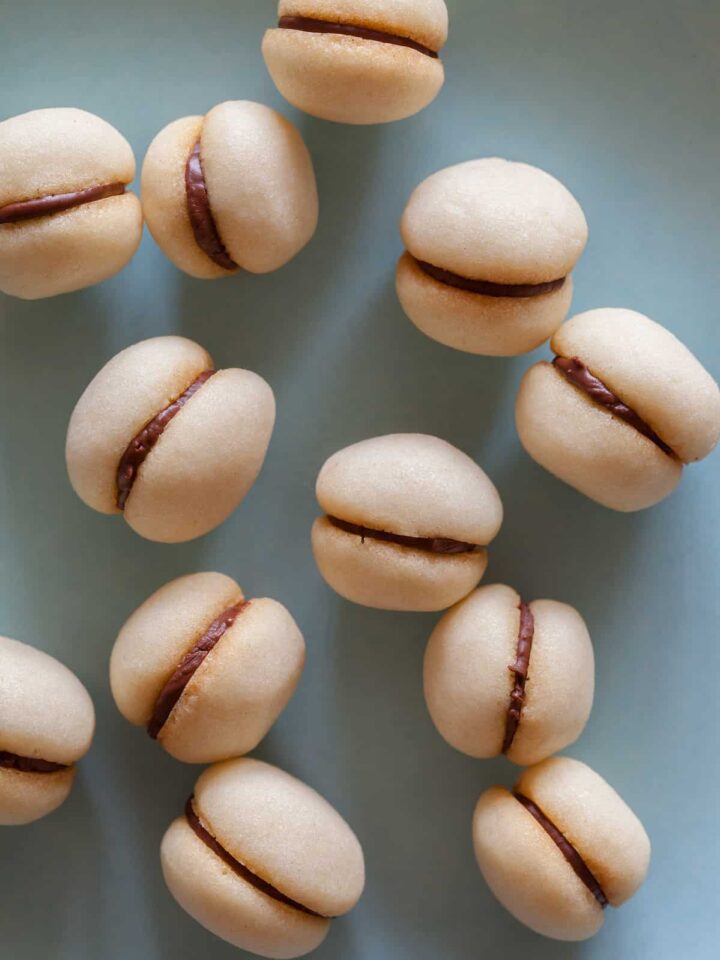 A close up of a bunch of baci di dama on a light blue surface.