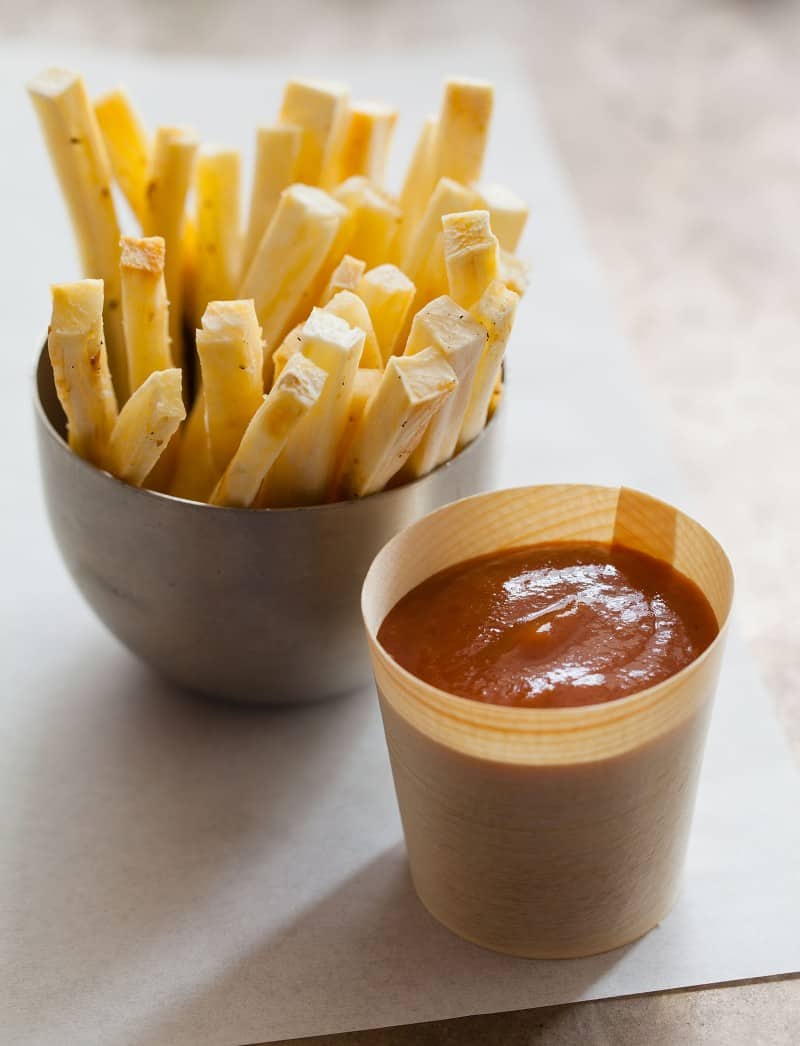 A bowl of baked yucca fries next to a cup of grilled banana ketchup.