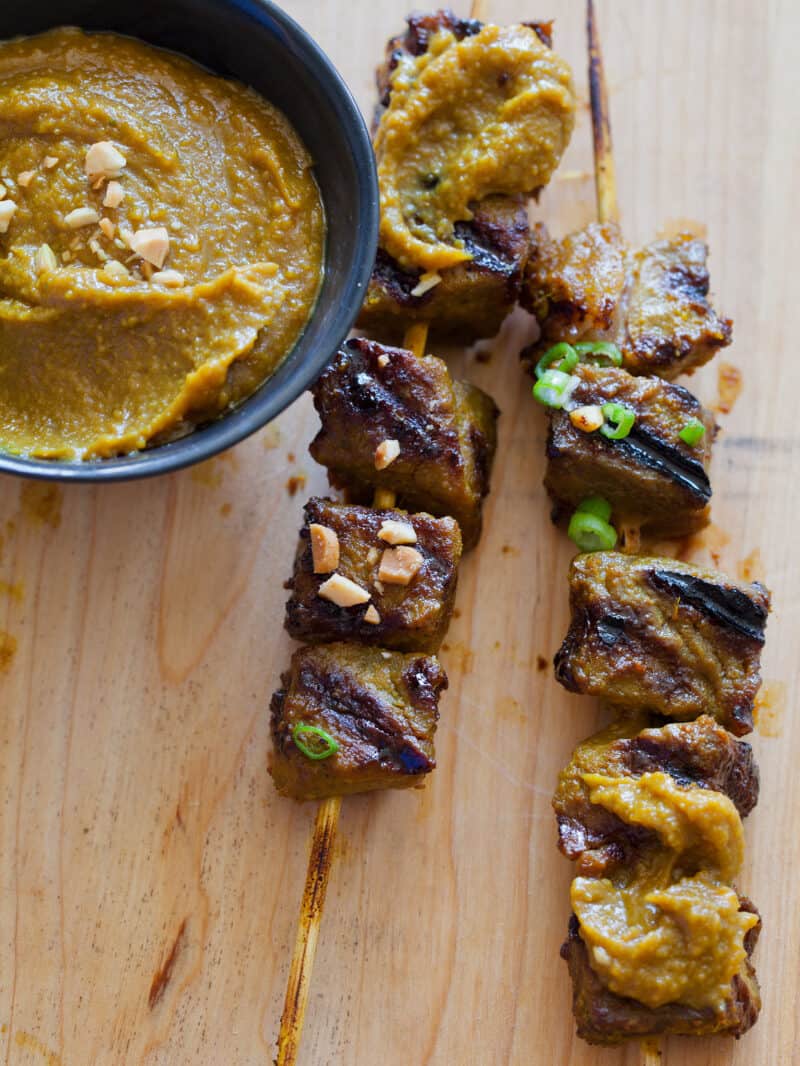 A close up of beef satay with a bowl of spicy peanut sauce.