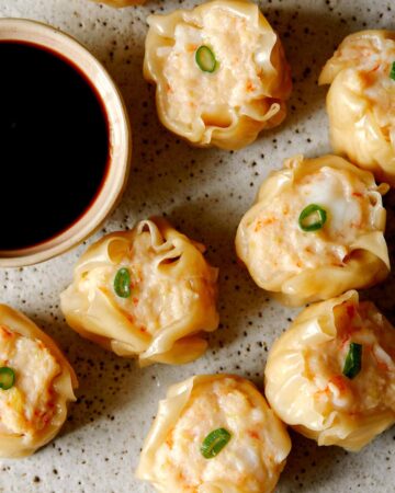 A close up of shrimp shumai with sauce on the side.