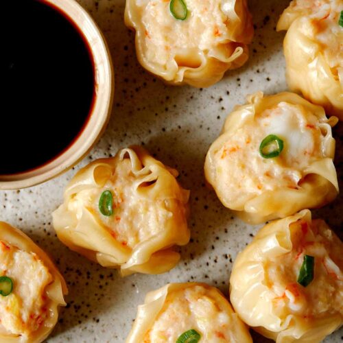 A close up of shrimp shumai with sauce on the side.