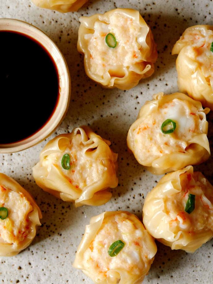A close up of shrimp shumai with sauce on the side.