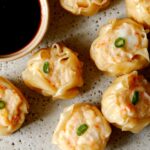 A close up of shrimp shumai with sauce on the side.