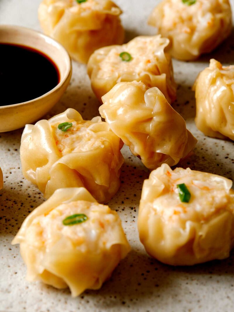 3/4 angle of 8 finished shrimp shumai next to ramekin of dipping sauce