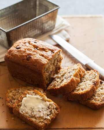 A sliced loaf of chocolate chip coconut banana bread with a knife and the empty pan.
