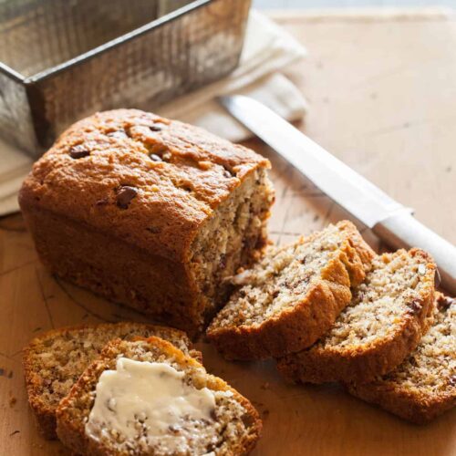 A sliced loaf of chocolate chip coconut banana bread with a knife and the empty pan.