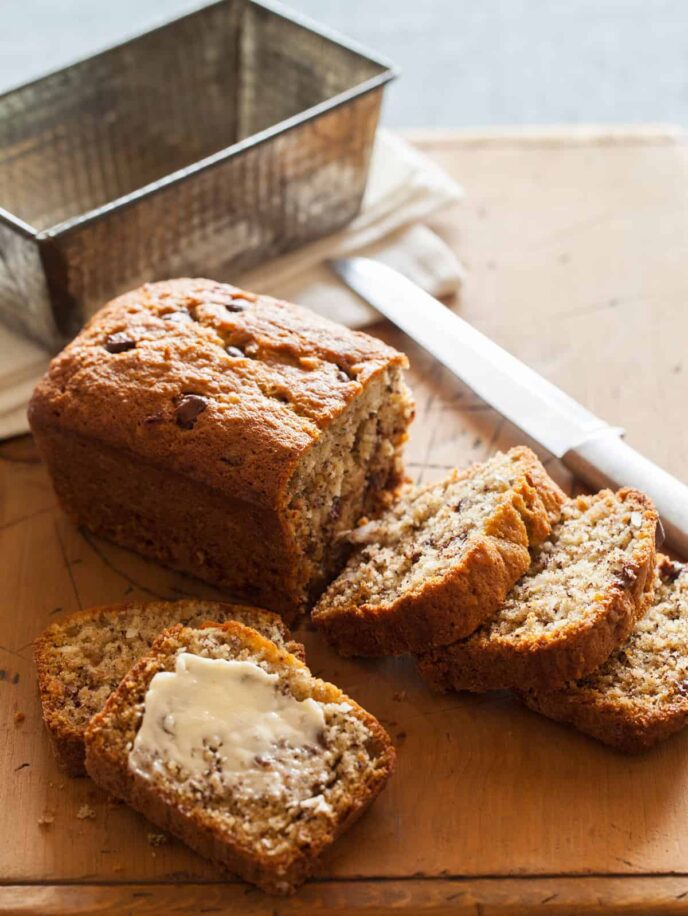 A sliced loaf of chocolate chip coconut banana bread with a knife and the empty pan.