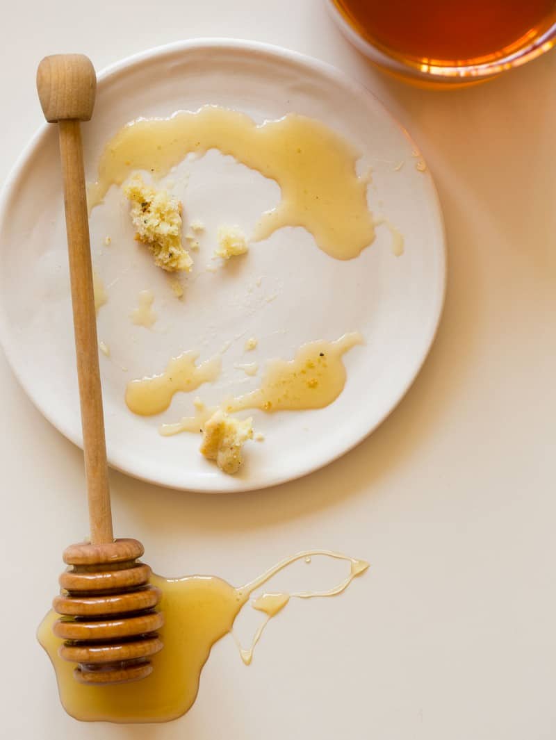 A white plate with honey and crumbs and a honey dipper.