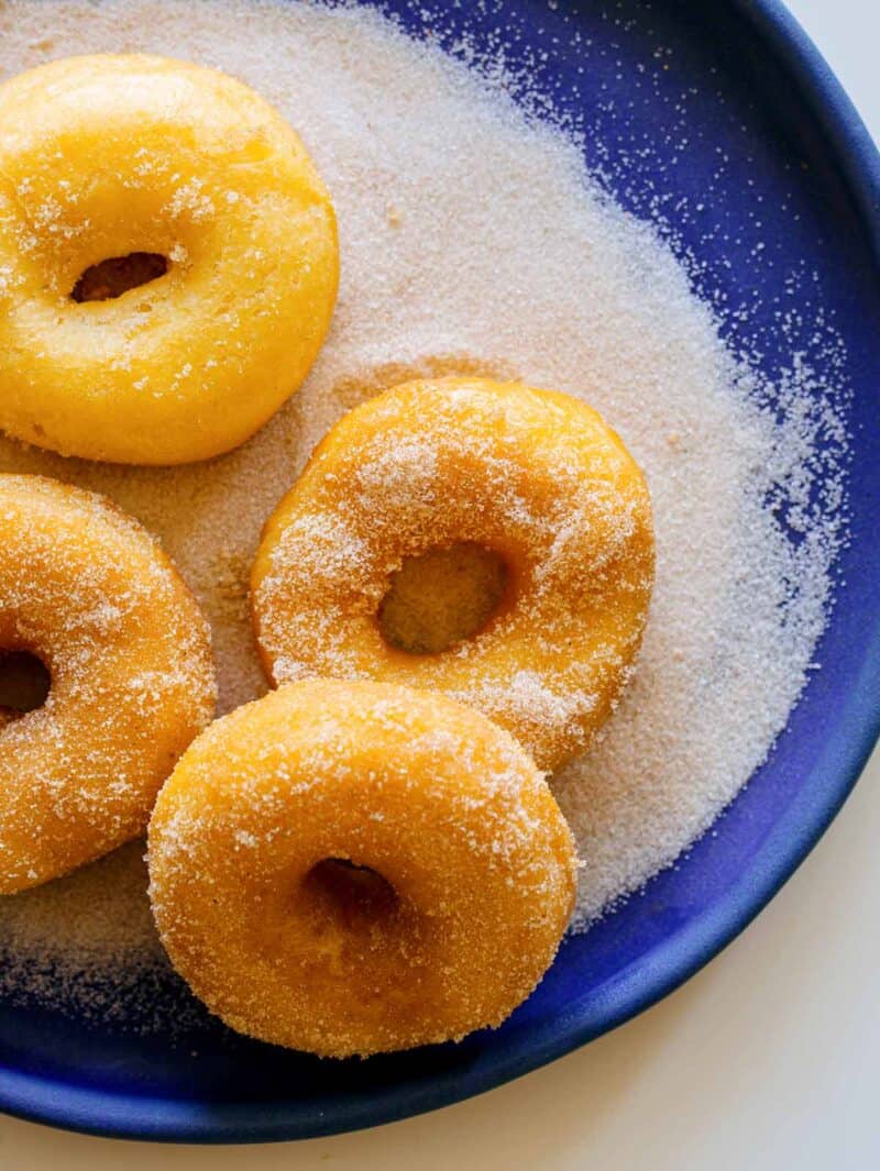 Spudnuts sitting on a plate of sugar.