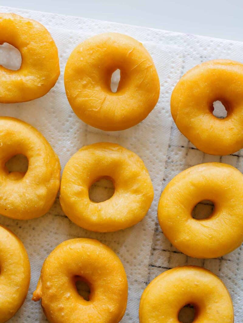 Several sweet potato spudnuts on a paper towel covered wire rack.