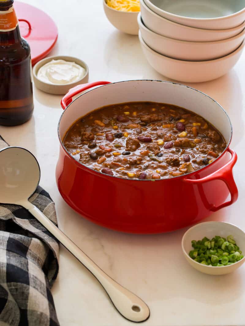 A pot of kitchen sink chili with extra bowls, a ladle, and ramekins of toppings.