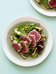 A bowl of black sesame and almond crusted ahi tuna on mixed greens with beech mushrooms.