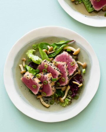 A bowl of black sesame and almond crusted ahi tuna on mixed greens with beech mushrooms.