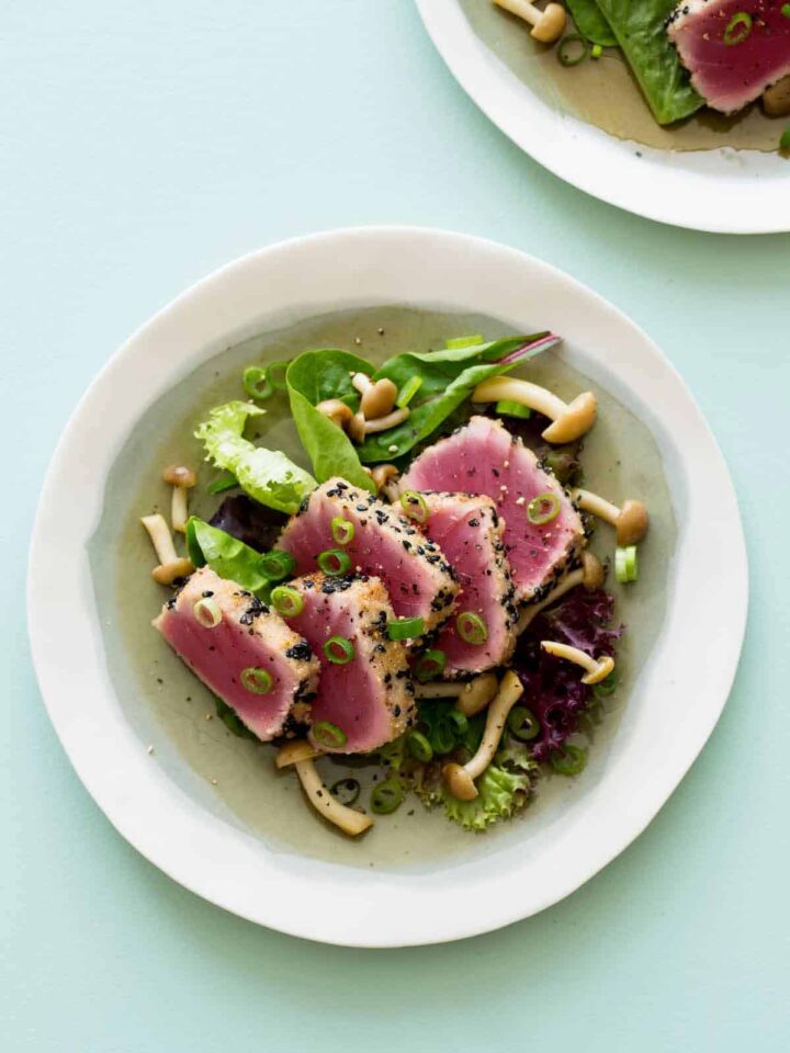 A bowl of black sesame and almond crusted ahi tuna on mixed greens with beech mushrooms.