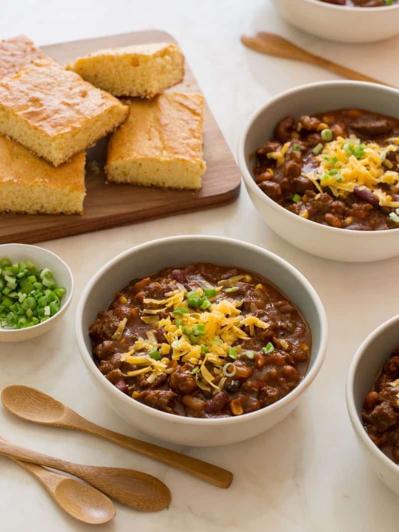 Several bowls of kitchen sink chili topped with cheese and green onion with cornbread.