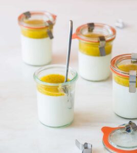 Several glass jars of vanilla bean panna cotta with mango coulis with a spoon.