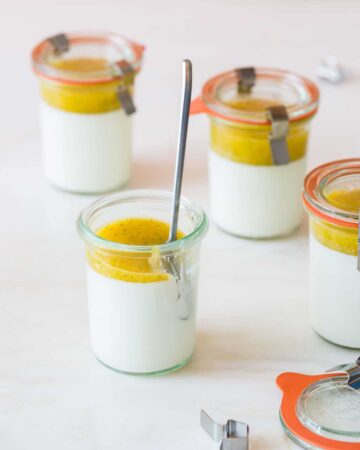 Several glass jars of vanilla bean panna cotta with mango coulis with a spoon.