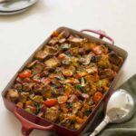 A baking pan of savory bread pudding with a large serving spoon.