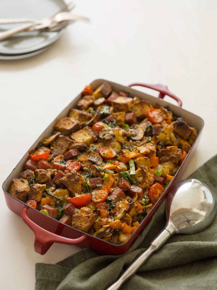 A baking pan of savory bread pudding with a large serving spoon.