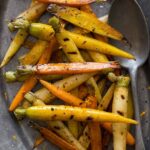 A plate of balsamic grilled baby carrots with a spoon.