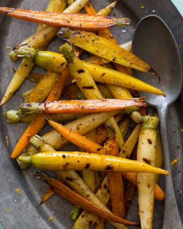 A plate of balsamic grilled baby carrots with a spoon.