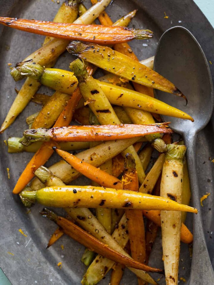 A plate of balsamic grilled baby carrots with a spoon.