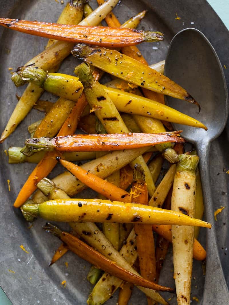 A plate of grilled baby carrots with a spoon.