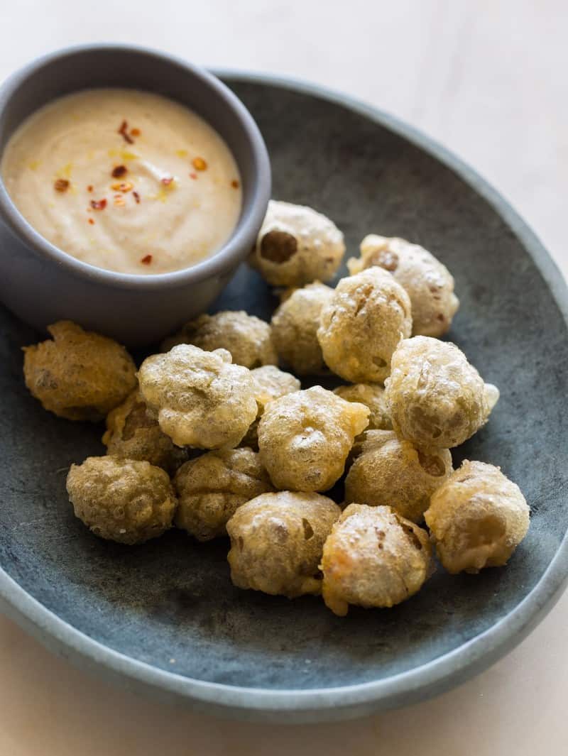 A close up of beer battered fried olives with a ramekin of cumin yogurt sauce.